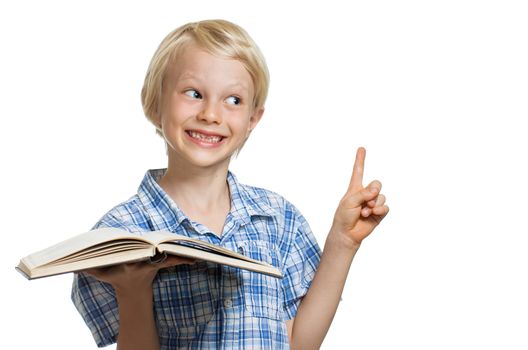A cute smiling young boy holding a book and pointing to copy-space. Isolated on white.