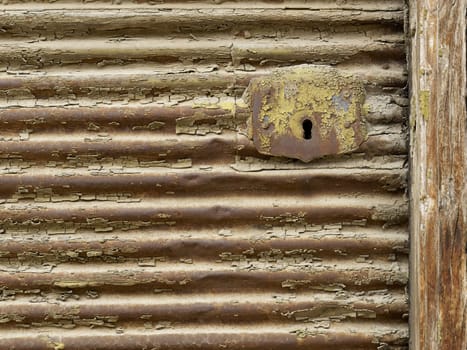 Key hole on old rusted metal shutter and wooden frame