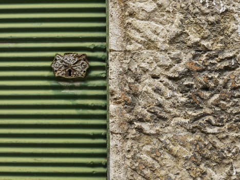 Key hole on old green metal shutter and stone wall      