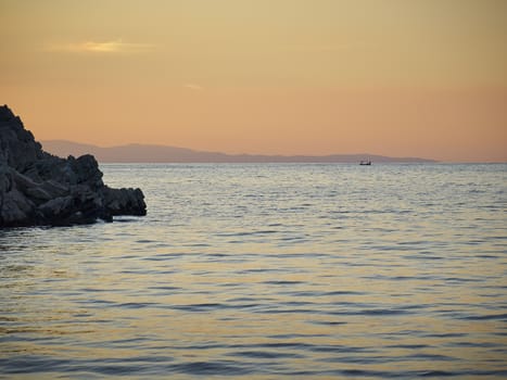 Sea​​, rock and distant fishermen at sunset