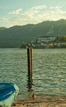 View of a lake with two wooden poles, a ship, a duck and an island