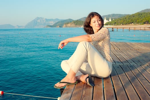 girl sitting on a pier near the sea and looking to the side