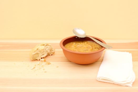 Spoon resting on a bowl of vegetable soup, with half a bread roll and a serviette