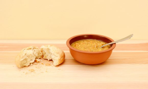 Bowl of delicious vegetable soup with a bread roll torn in half