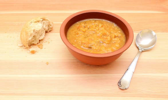 Half-eaten crusty bread roll with a bowl of chunky vegetable soup