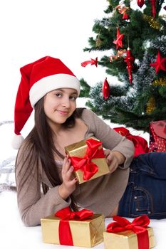 Smiling teen girl in Santa hat with gifts under Christmas tree