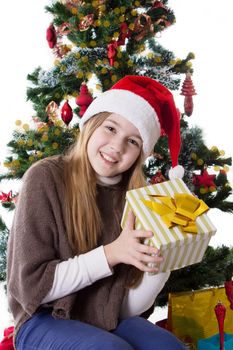 Cute teenage girl in Santa hat with present under Christmas tree