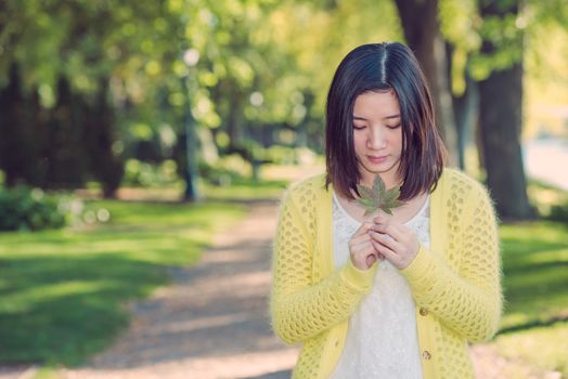 Portrait of young attractive woman holding a leaf close to mouth at an end of a road