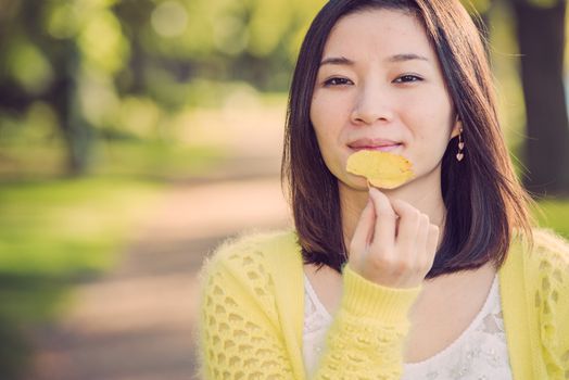 Portrait of young attractive woman holding a leaf close to mouth at an end of a road