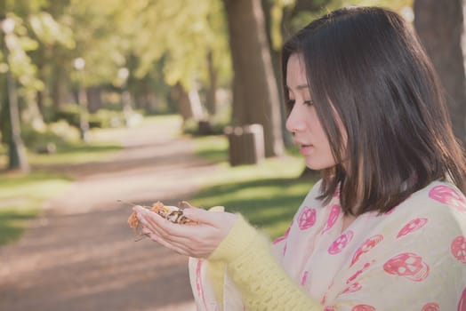 Cute young girl holding a handful of leafs at the end of a park road