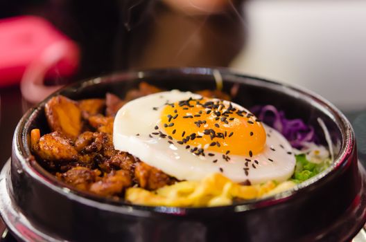 closeup bibimbap with fried egg in a heated stone bowl ,  korean style food