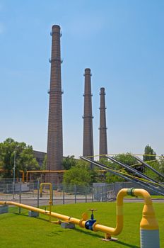 Image of a gas pipeline in background of three old brick chimneys.