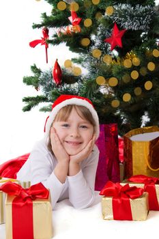 Smiling girl in Santa hat lying under Christmas tree