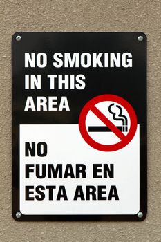 Bilingual no smoking sign with graphic and written in the English and Spanish languages is screwed to a wall.
