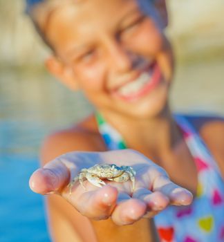 Adorable happy girl holding crab on hand on the beach. Focus on the crab.