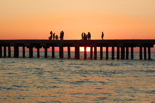 Groups of people on the old pier admire the beautiful sunset over the Black Sea coast in Crimea, Ukraine