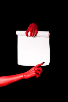 Red devil hands holding paper scroll and pointing at signature place, isolated on black background 