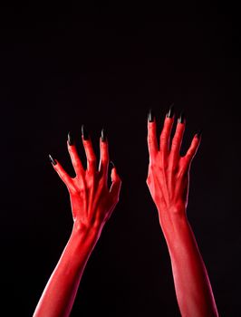 Red spooky devil hands with black nails, Halloween theme, studio shot on black background 