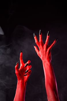 Spooky red devil hands with black nails on smoky background, studio shot 