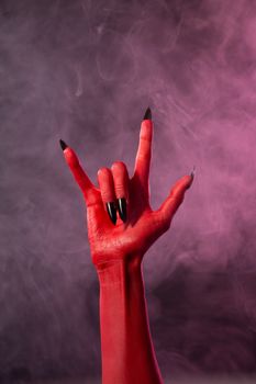 Heavy metal, red devil hand with black nails, studio shot on smoky background 