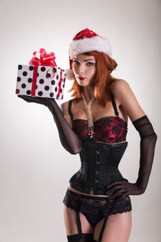 Pretty girl wearing pinup outfit and Santa Claus hat, holding gift box, Christmas theme 