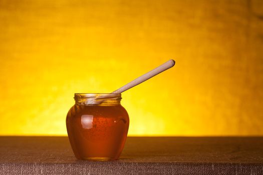 Honey jar on canvas table, studio shot over warm background 