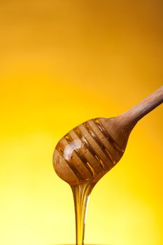 Close-up shot of wooden dipper and flowing honey over yellow background 