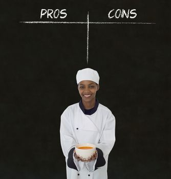 African American woman chef holding soup bowl with chalk pros and cons on blackboard background