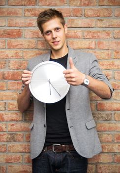 Young businessman holding a clock on brick wall background. Time in business concept