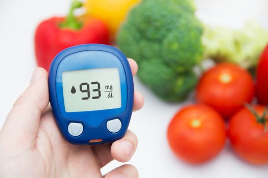 Hand holding meter. Diabetes doing glucose level test. Vegetables in background