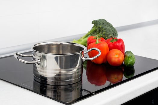 Pot and vegetables in modern kitchen with induction stove