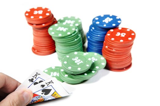 Cards in the human hand and numerous poker chips on a white table
