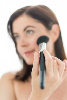 portrait of a beautiful mature lady using professional brush to apply powder on her cheekbones