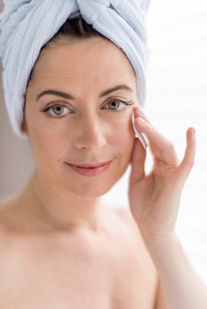 portrait of a beautiful mature lady using cotton pads to clean her skin and remove make up