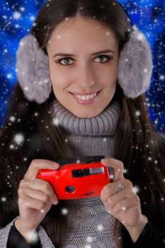 Beautiful girl holding a photo camera with snow falling around her.