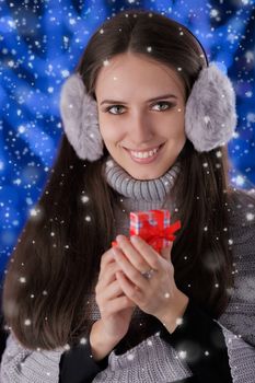 Beautiful girl holding a small gift box with snow falling around her.