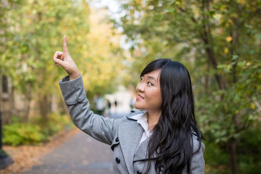 Portrait of young attractive girl pointing at something on the trees at the side of a road