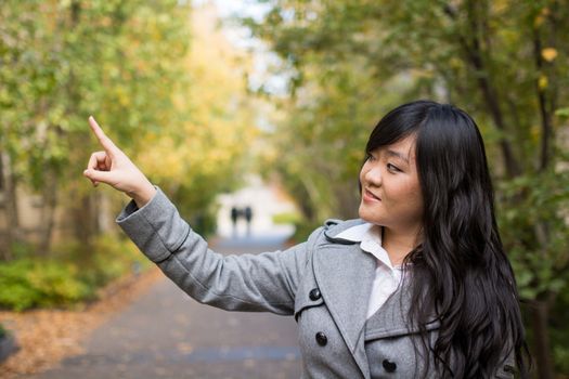 Portrait of young attractive girl pointing at something on the trees at the side of a road