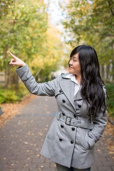 Portrait of young attractive girl pointing at something on the trees at the side of a road