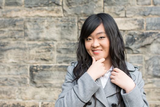 Portrait of beautiful young girl in front of a stone wall looking happy