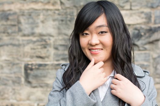 Portrait of beautiful young girl in front of a stone wall looking happy