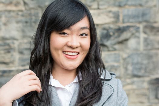 Portrait of beautiful young girl in front of a stone wall looking happy