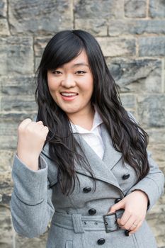 Portrait of successful young woman in front of a stone wall holding up fist