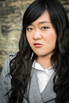 Portrait of young woman in front of a stone wall looking angry