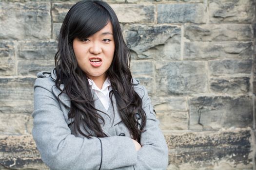 Portrait of young woman in front of a stone wall looking angry with arms crossed