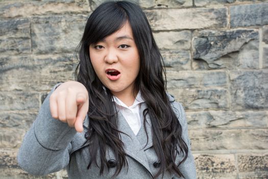 Portrait of young woman in front of a stone wall looking angry