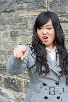 Portrait of young woman in front of a stone wall looking angry