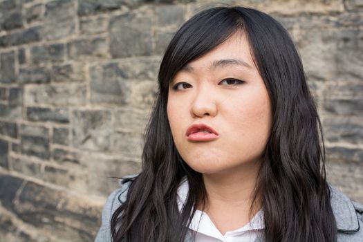 Portrait of young woman in front of a stone wall looking angry