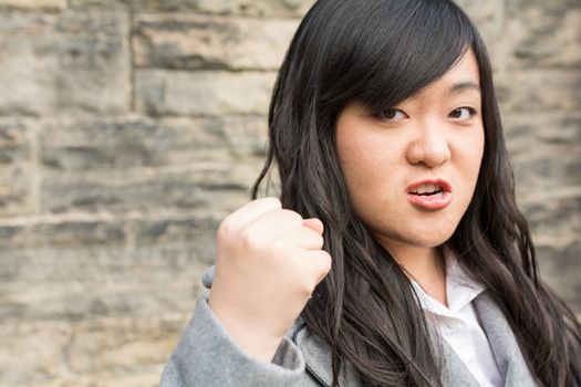 Portrait of young aggressive woman in front of a stone wall looking angry and holding fist