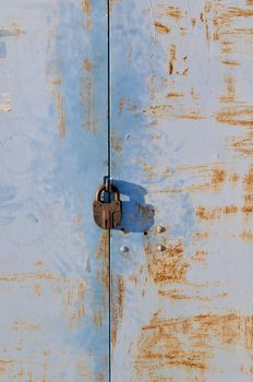 Old rusty padlock on blue weathered metal gate